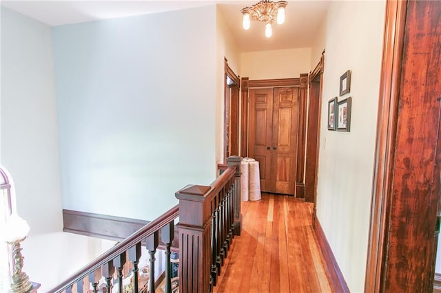 corridor with light wood finished floors, a chandelier, and an upstairs landing