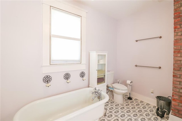 bathroom with toilet, tile patterned flooring, baseboards, and a freestanding bath