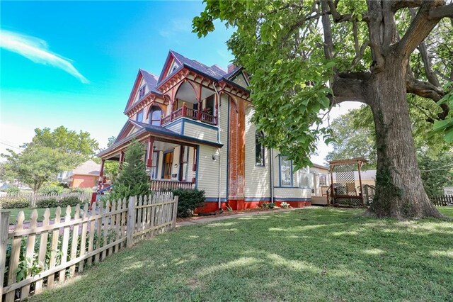 back of property featuring a balcony, a chimney, fence, and a yard