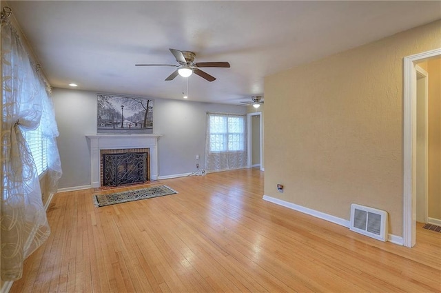 unfurnished living room featuring a fireplace with raised hearth, wood-type flooring, visible vents, and baseboards