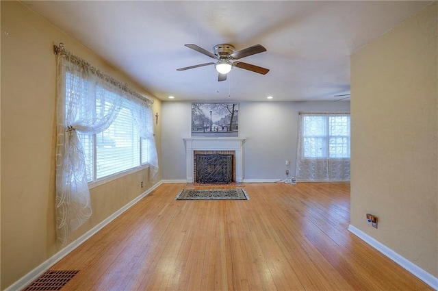 unfurnished living room featuring ceiling fan, a fireplace with flush hearth, visible vents, baseboards, and wood-type flooring