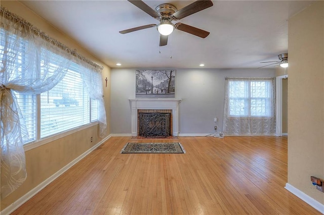 unfurnished living room with a fireplace with flush hearth, a healthy amount of sunlight, baseboards, and hardwood / wood-style flooring