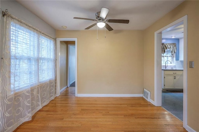 spare room featuring visible vents, a sink, ceiling fan, light wood-type flooring, and baseboards