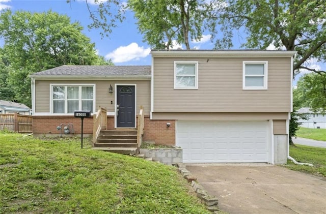 split level home featuring a garage, concrete driveway, fence, a front lawn, and brick siding