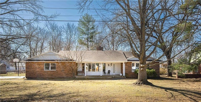 ranch-style home with brick siding, a porch, a chimney, and a front yard