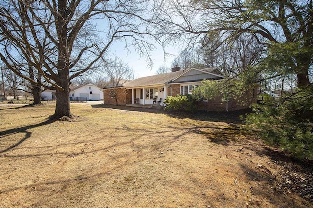 rear view of house featuring brick siding, covered porch, a chimney, and a yard