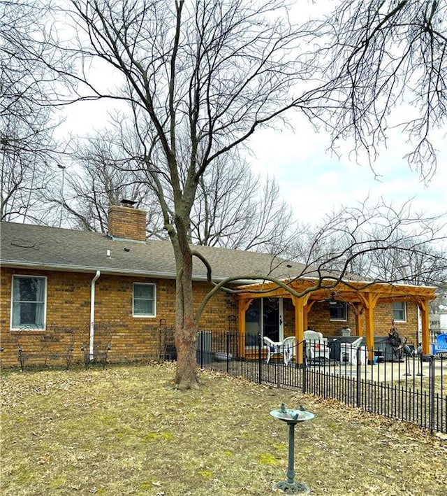 rear view of house with brick siding, a patio area, fence, and a chimney