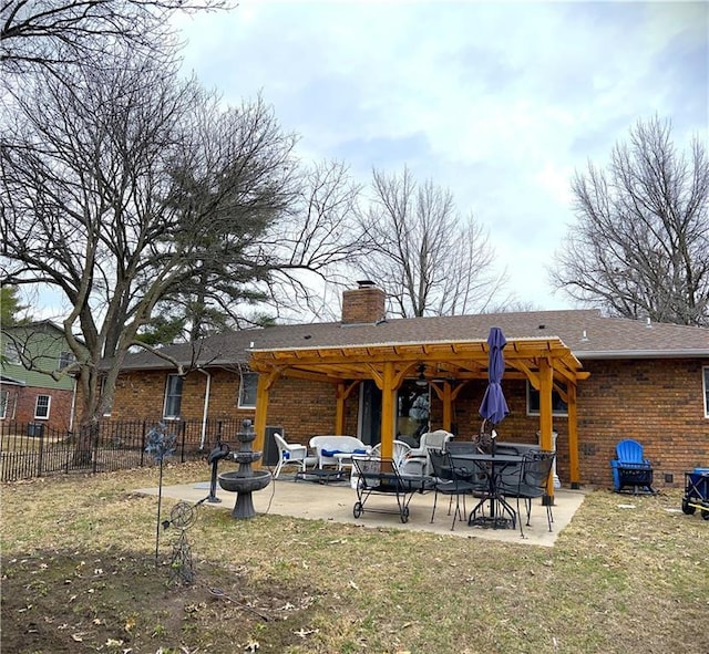 rear view of house featuring a lawn, a patio, fence, brick siding, and a chimney