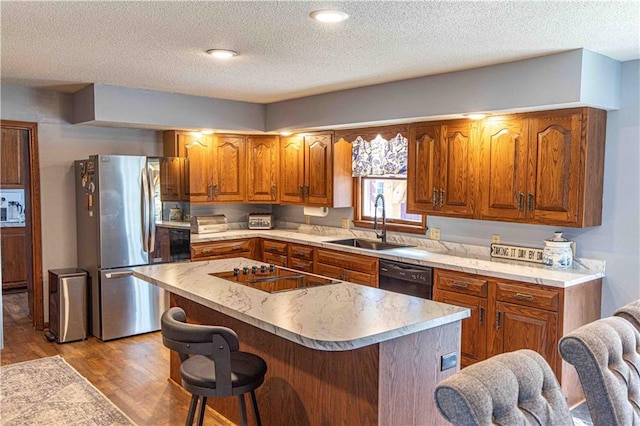 kitchen featuring wood finished floors, brown cabinetry, a sink, black appliances, and a center island