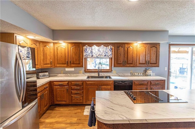 kitchen with a sink, black appliances, brown cabinetry, and light countertops