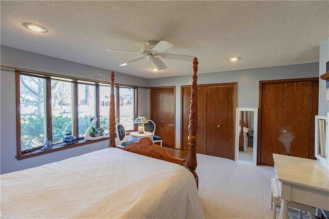 bedroom featuring carpet floors, a textured ceiling, ceiling fan, and multiple closets