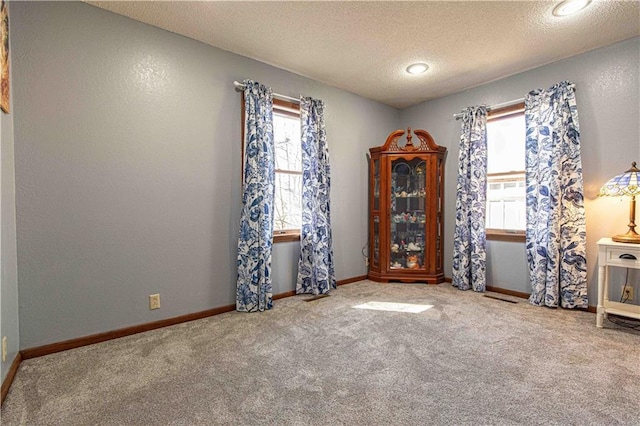 spare room featuring carpet flooring, a textured ceiling, baseboards, and a textured wall