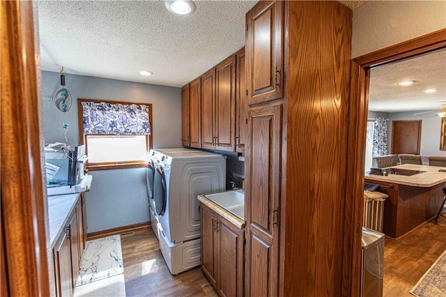 clothes washing area featuring a textured ceiling, cabinet space, wood finished floors, and washer and clothes dryer