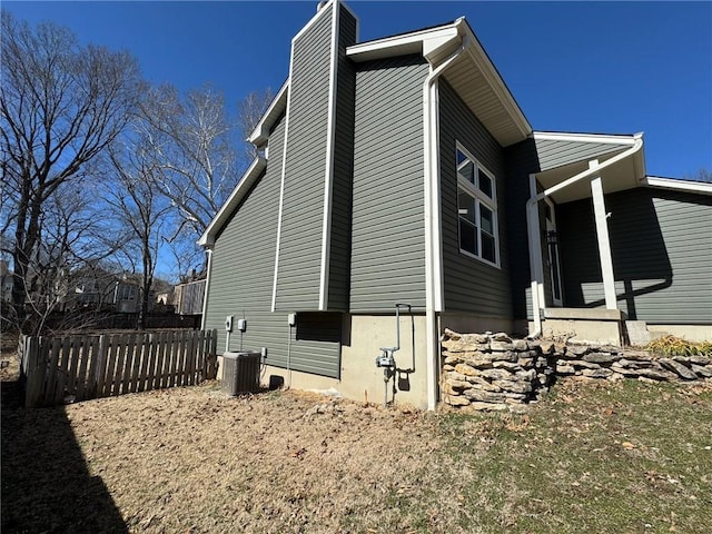 view of home's exterior featuring a chimney, fence, and central AC