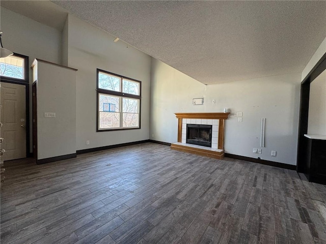 unfurnished living room with a textured ceiling, baseboards, dark wood-type flooring, and a tile fireplace