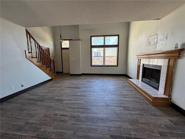 unfurnished living room featuring baseboards, a textured ceiling, a tiled fireplace, and wood finished floors