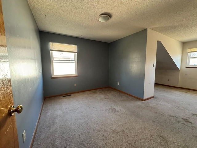 interior space with a textured ceiling, carpet flooring, visible vents, and baseboards