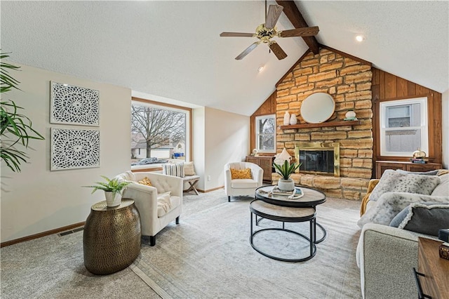 living area with vaulted ceiling with beams, a textured ceiling, a stone fireplace, carpet flooring, and baseboards