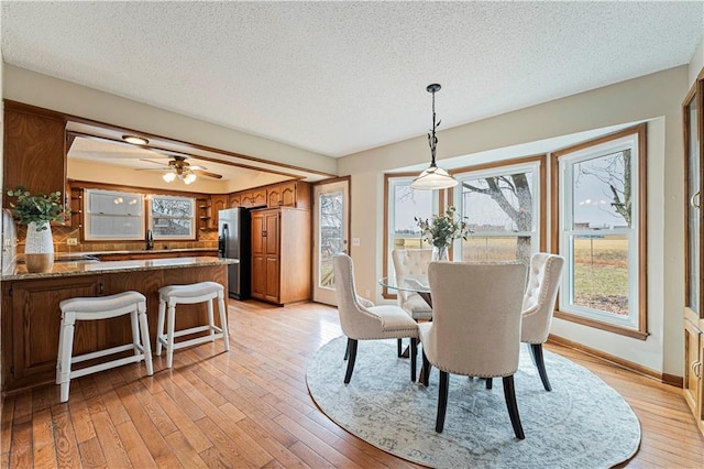 dining space with light wood-type flooring, a textured ceiling, and baseboards