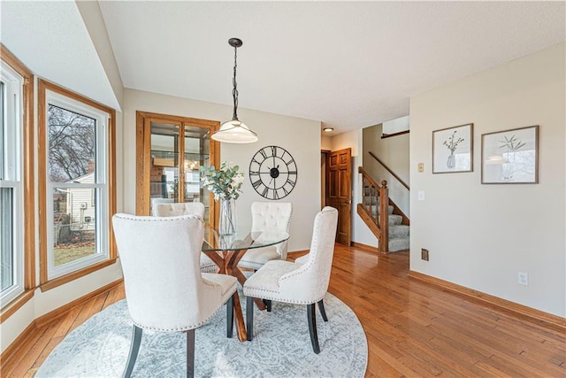 dining space with baseboards, light wood finished floors, and stairs