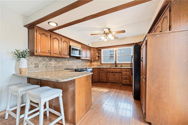 kitchen featuring a peninsula, brown cabinets, stainless steel appliances, and decorative backsplash