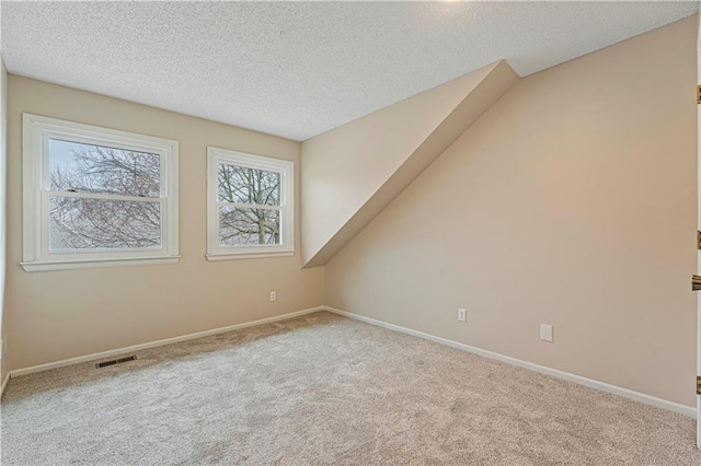 additional living space with carpet floors, visible vents, a textured ceiling, and baseboards