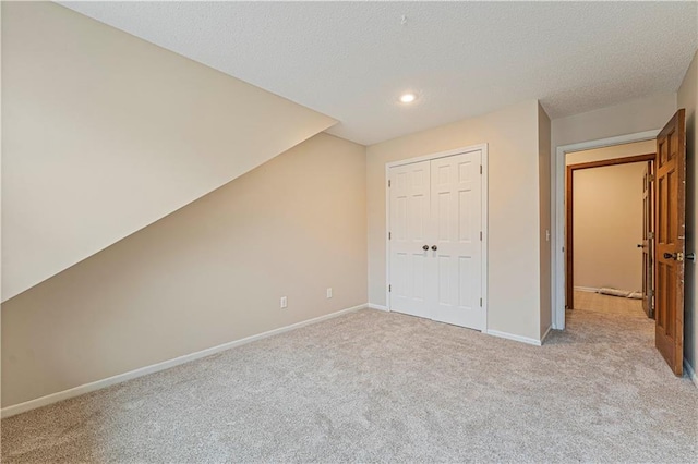 unfurnished bedroom with recessed lighting, a closet, light carpet, a textured ceiling, and baseboards