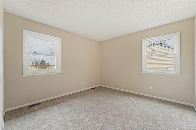 empty room with visible vents, plenty of natural light, and carpet flooring