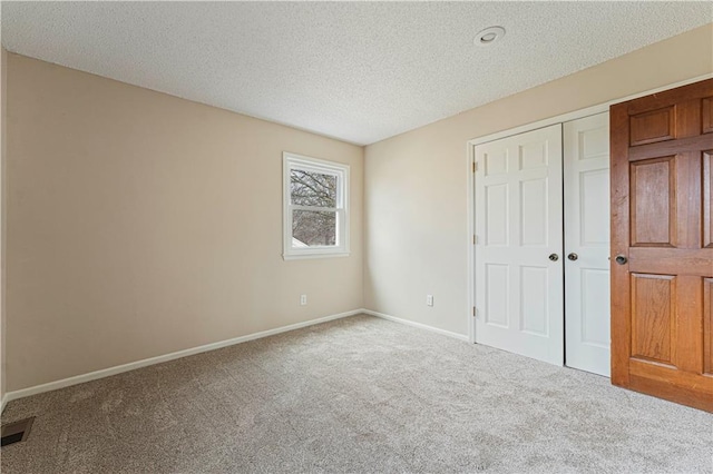 unfurnished bedroom featuring carpet floors, a closet, a textured ceiling, and baseboards