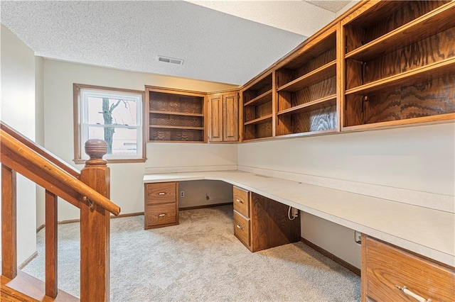 unfurnished office with a textured ceiling, light colored carpet, visible vents, baseboards, and built in study area