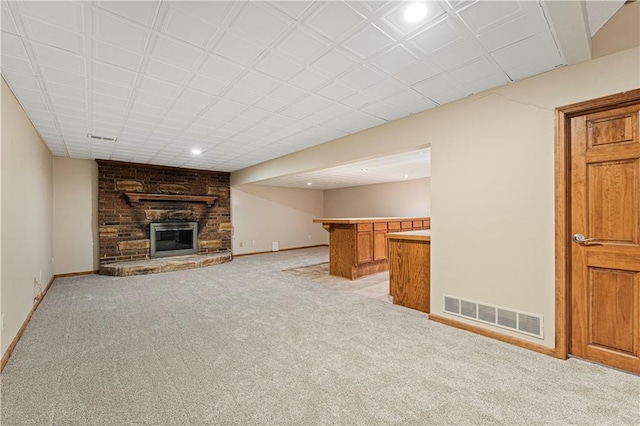 unfurnished living room with light colored carpet, a brick fireplace, visible vents, and baseboards