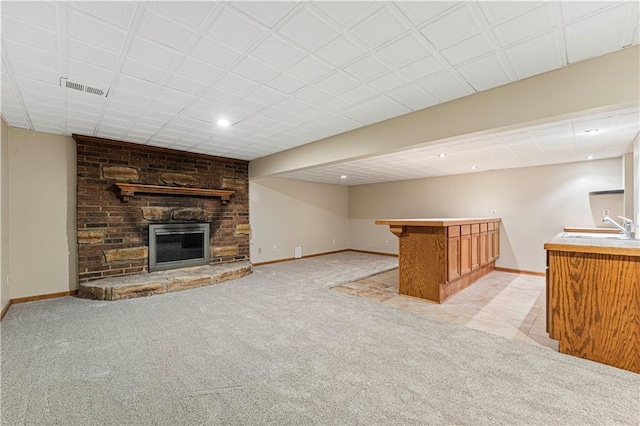 unfurnished living room with light colored carpet, a brick fireplace, a sink, a bar, and baseboards