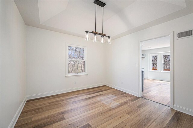 unfurnished dining area featuring baseboards, visible vents, a raised ceiling, and wood finished floors