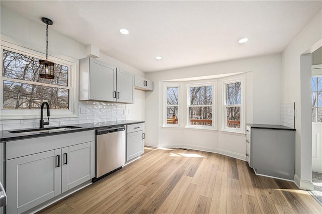 kitchen with a sink, dark countertops, light wood-type flooring, and dishwasher