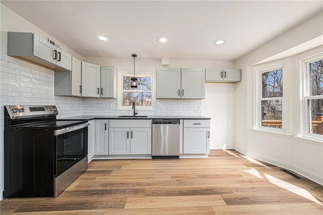 kitchen featuring light wood finished floors, stainless steel appliances, dark countertops, visible vents, and a sink