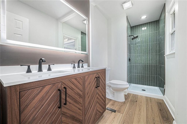 full bathroom with toilet, a tile shower, a sink, and wood finished floors