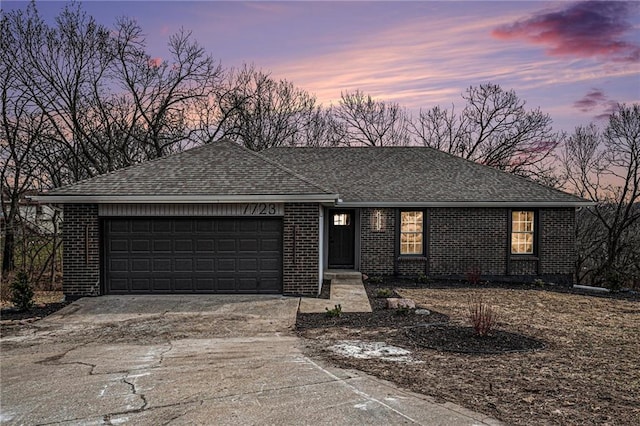 single story home with a garage, driveway, a shingled roof, and brick siding