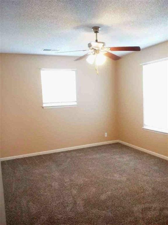 carpeted empty room with visible vents, a healthy amount of sunlight, a textured ceiling, and a ceiling fan