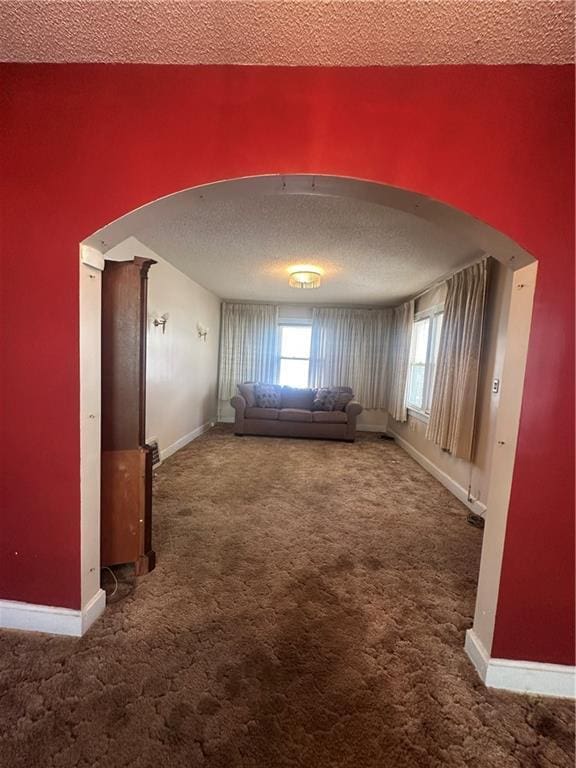 unfurnished living room featuring arched walkways, a textured ceiling, plenty of natural light, and carpet flooring