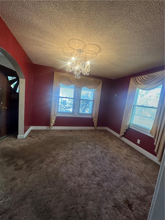 unfurnished dining area with arched walkways, carpet, a chandelier, and a wealth of natural light