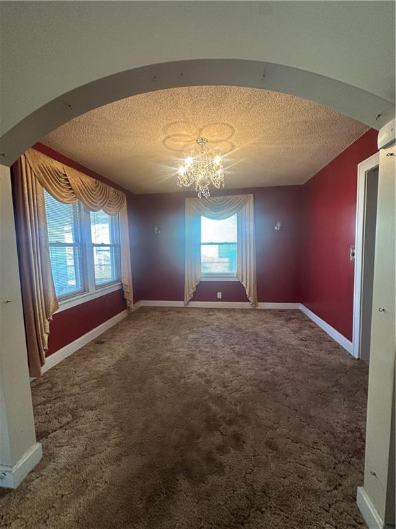 carpeted spare room featuring arched walkways, a notable chandelier, a textured ceiling, and baseboards