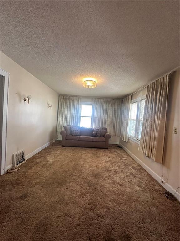 unfurnished living room featuring carpet floors, a textured ceiling, and baseboards