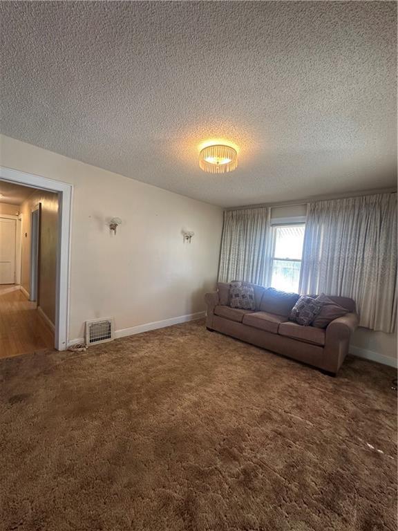 unfurnished living room with a textured ceiling, carpet flooring, visible vents, and baseboards