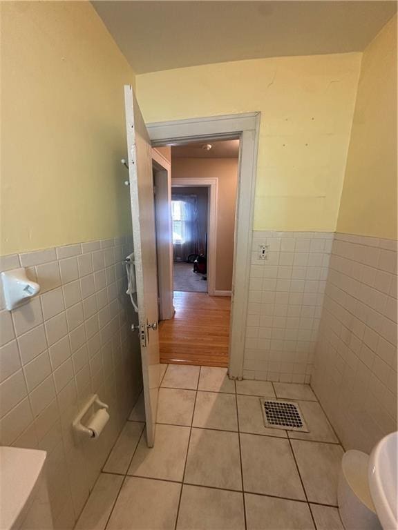 half bathroom with a wainscoted wall, visible vents, tile walls, and tile patterned floors