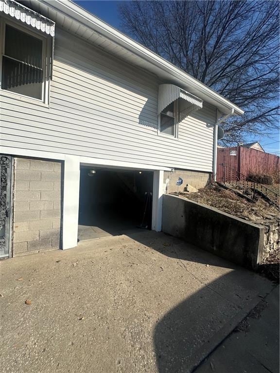 view of property exterior with driveway, an attached garage, and fence