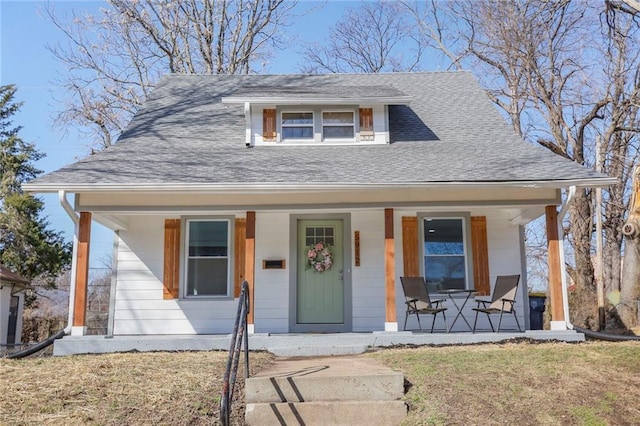 bungalow-style house featuring covered porch, a shingled roof, and a front yard