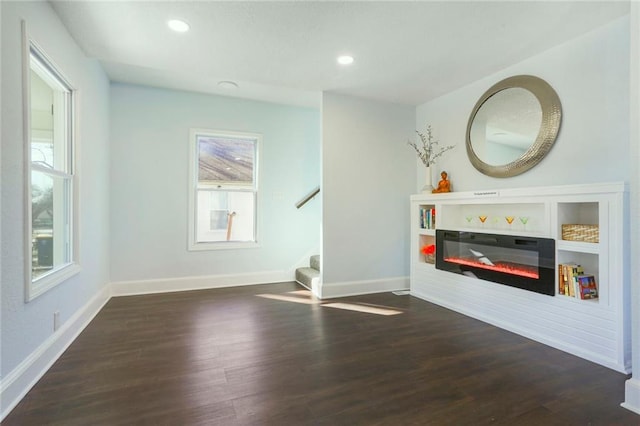 interior space featuring baseboards, a glass covered fireplace, wood finished floors, stairs, and recessed lighting