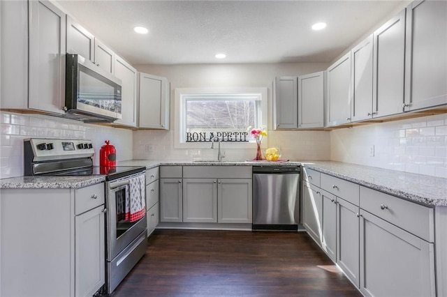 kitchen featuring light stone counters, dark wood-style flooring, decorative backsplash, appliances with stainless steel finishes, and a sink