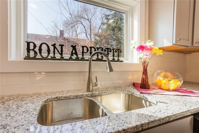 room details featuring backsplash, a sink, and light stone countertops