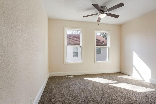 carpeted spare room featuring a textured wall and baseboards